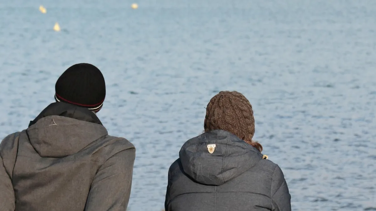 Zwei Menschen stehen mit Abstand nebeneinander am Ufer eines Sees