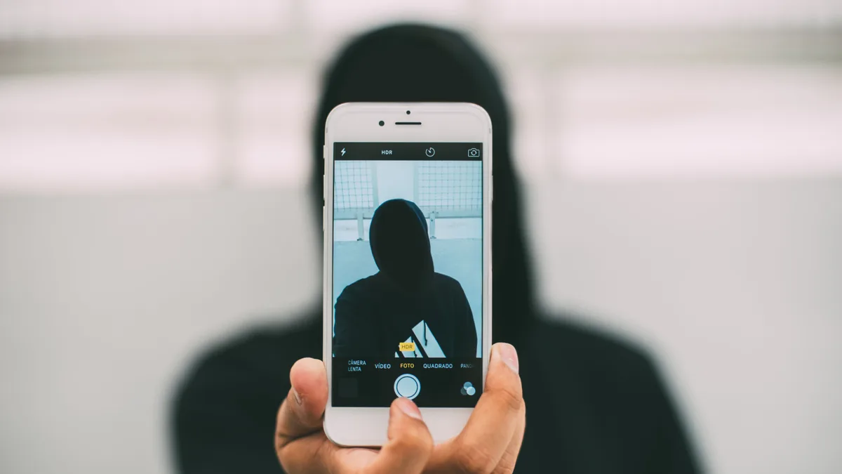 Person mit Kapuze hält ein Smartphone, das Gesicht bleibt im Dunkeln