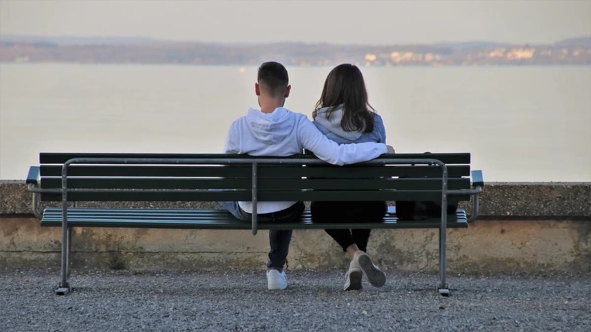 Paar sitzt schweigend nebeneinander auf einer Bank und blickt aufs Wasser